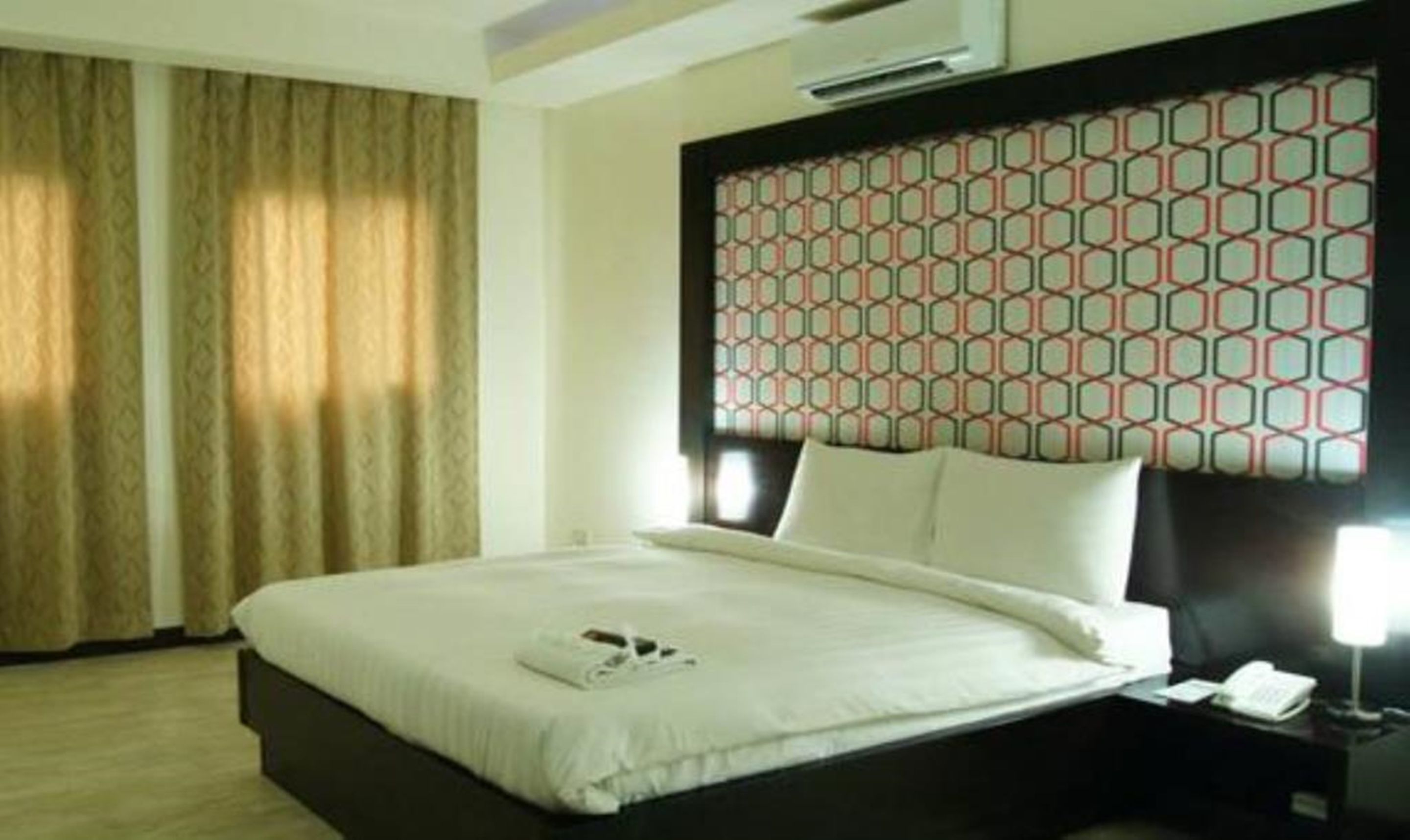 A hotel room with a bed, a nightstand, a lamp, and a window with curtains.