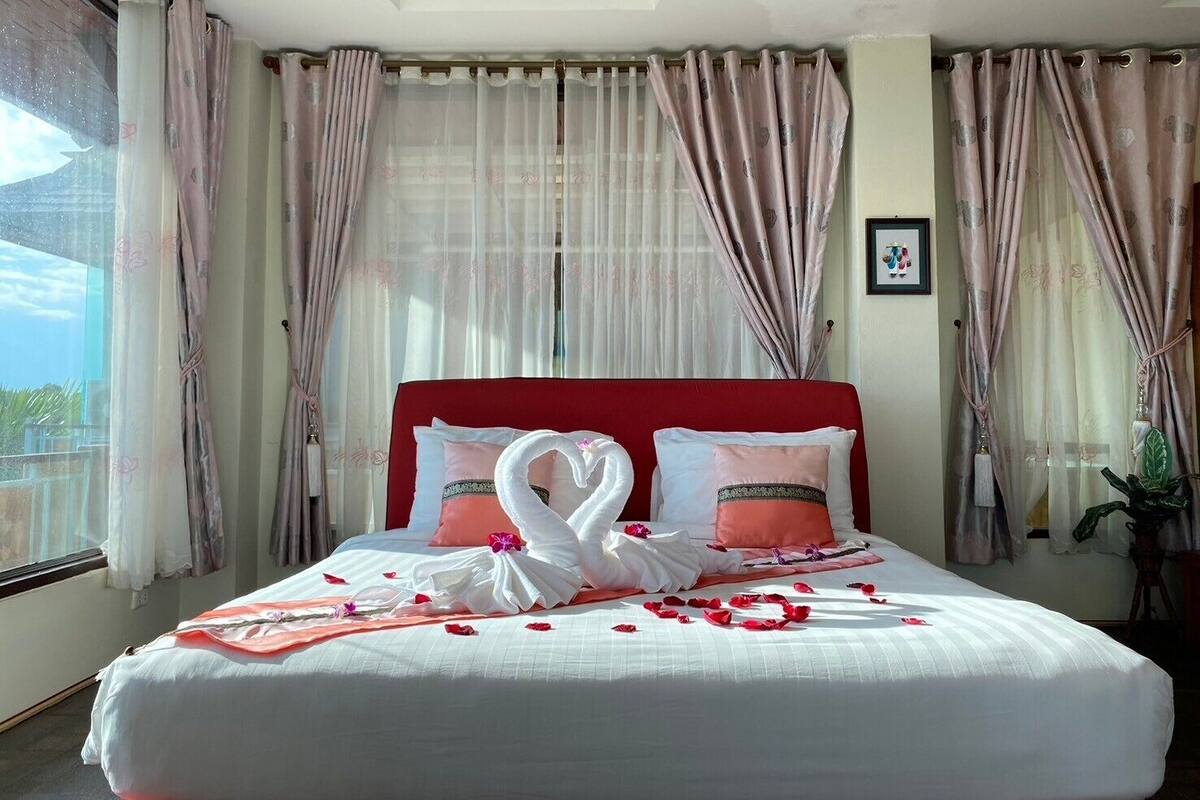 Habitación de hotel con una cama grande, cabecera roja y cortinas traslúcidas.