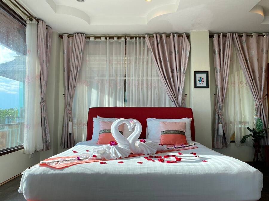 A hotel room with a large bed, red headboard, and sheer curtains.