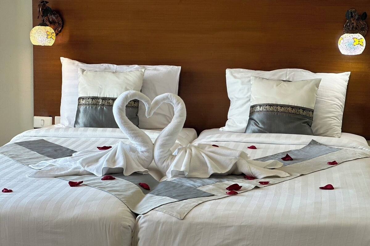 Habitación de hotel con una cama grande, dos almohadas y una presentación de toallas con forma de corazón.