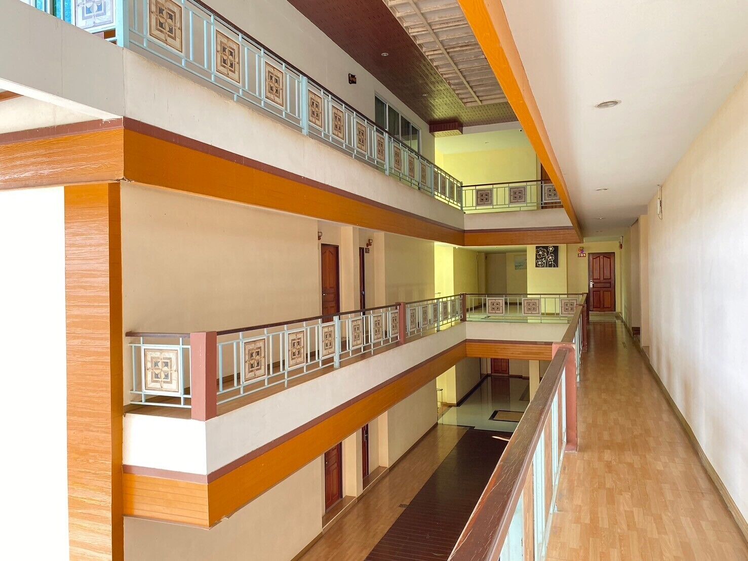 Un interior de varios niveles con suelos de madera, un espacio central abierto y balcones con barandillas.