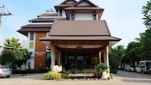 A multi-story building with a prominent entrance, a signboard, and a parking area with vehicles. - Chaophaya Thara Riverside (Chai Nat)