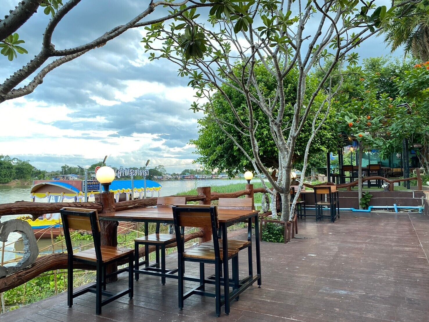 An outdoor dining area with wooden tables and chairs, overlooking a river.