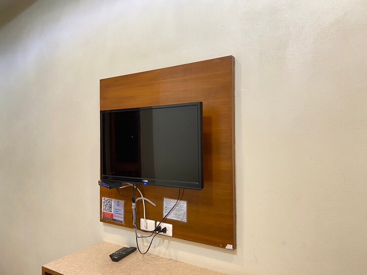 Televisor de pantalla plana montado en un panel de madera con un control remoto sobre una superficie color beige.