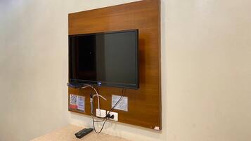 Televisor de pantalla plana montado en un panel de madera con un control remoto sobre una superficie color beige.