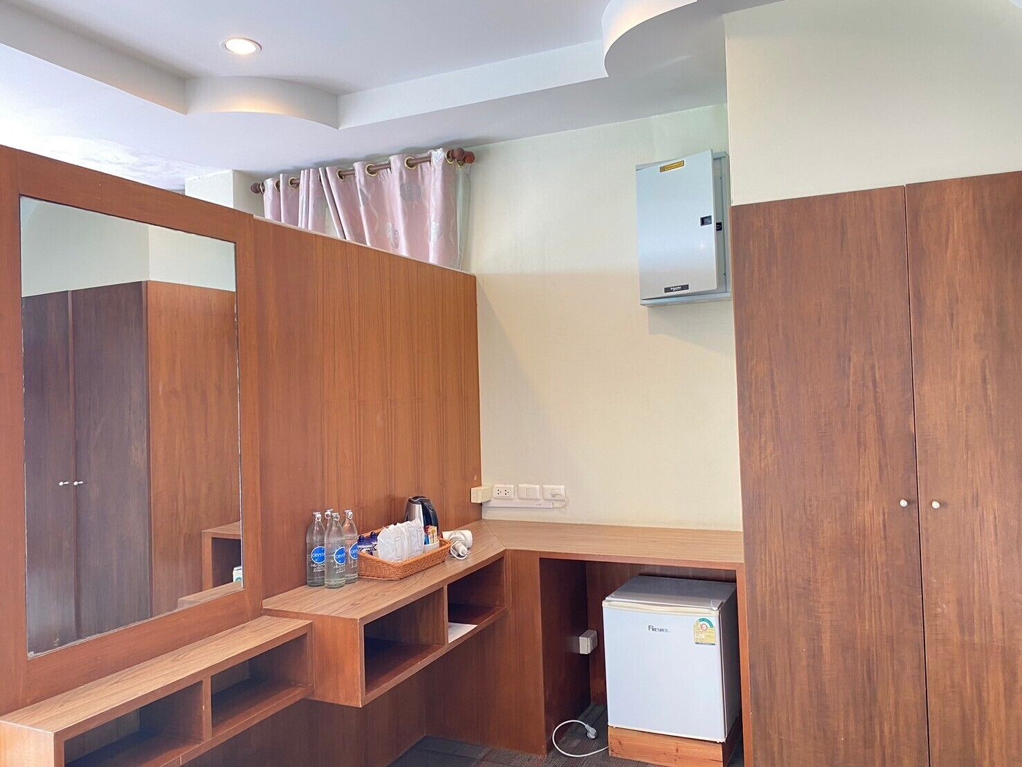 A compact bathroom with wooden cabinetry, a mirror, a small refrigerator, and a vanity with toiletries.