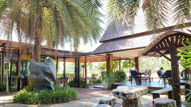 A covered outdoor seating area with stone tables and benches, surrounded by lush greenery and palm trees. - Chaophaya Thara Riverside (Chai Nat)