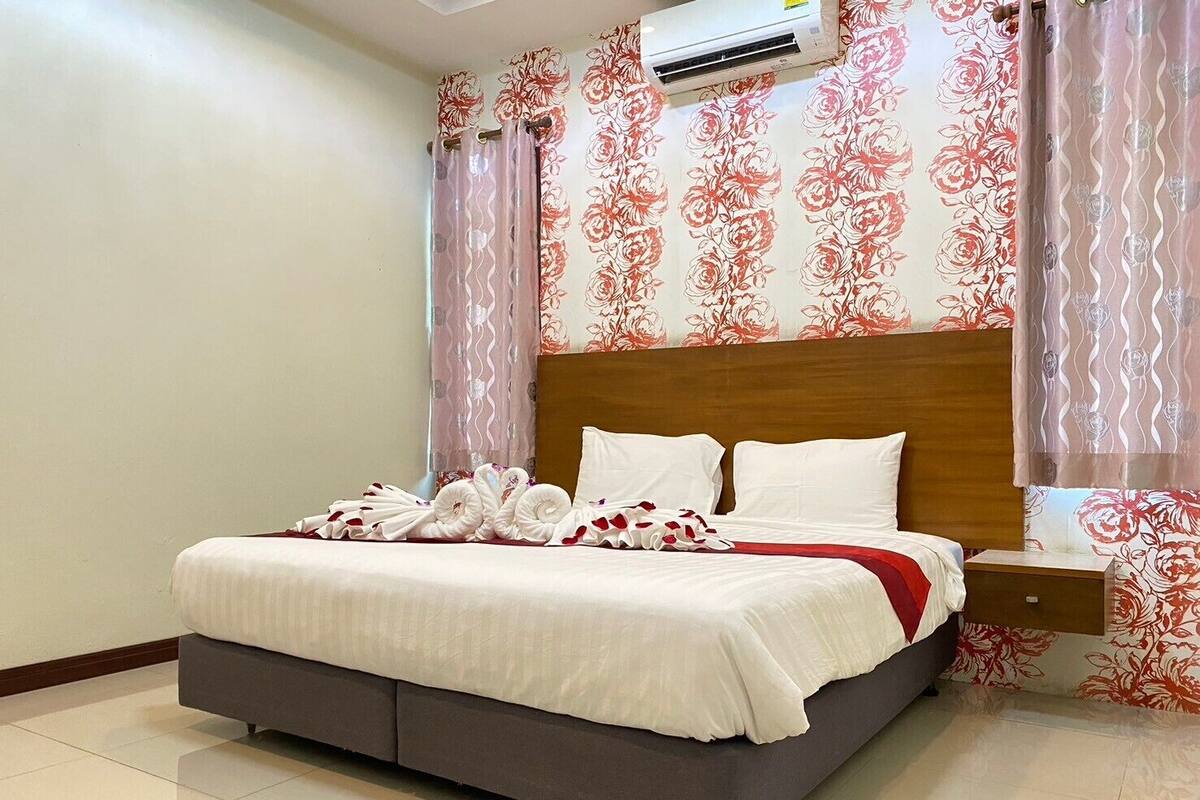 Una cama bien hecha con sábanas blancas, cabecera de madera y una almohada roja decorativa.