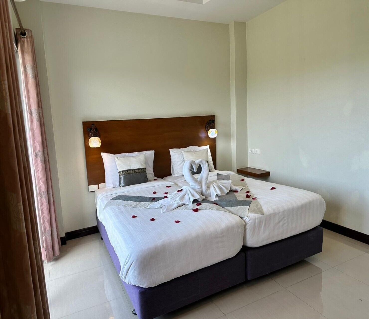 A double bed with a wooden headboard, white bedding, and rose petals on the bed.