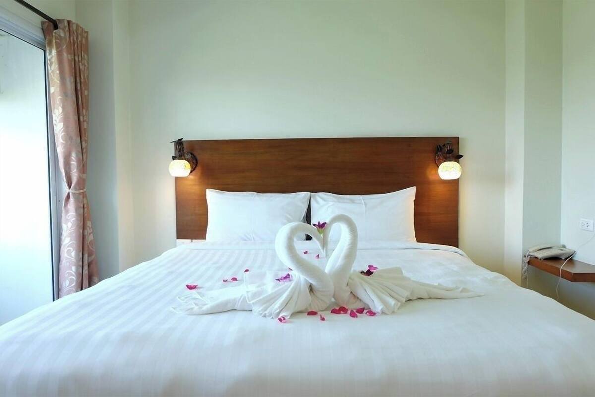 Una cama bien tendida con cabecera de madera, almohadas blancas y una decoración de toalla con forma de cisne.