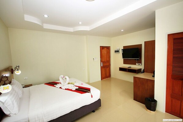 A hotel room with a bed, a TV, a desk, and a trash bin. - Chaophaya Thara Riverside (Chai Nat)
