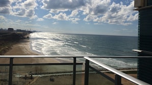 A coastal view from a balcony with a metal railing, overlooking a beach and ocean. - Okeanos ba Marina by Sophie (Herzliya)