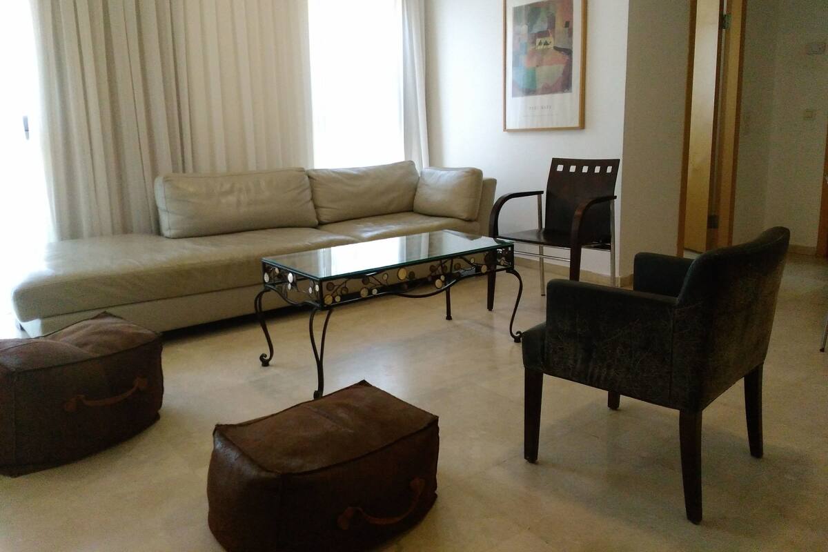 Ein Wohnzimmer mit einer Couch, einem Glastisch, einem Sessel und einem braunen Hocker.