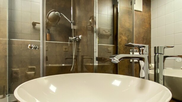 A modern bathroom with a large white freestanding sink, a glass-enclosed shower, and a separate vanity with a mirror. - IMPULSIV Hotel & Sportresort (Loerrach)