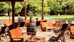 Outdoor seating with wooden tables and chairs, surrounded by sand and trees. - IMPULSIV Hotel & Sportresort (Loerrach)
