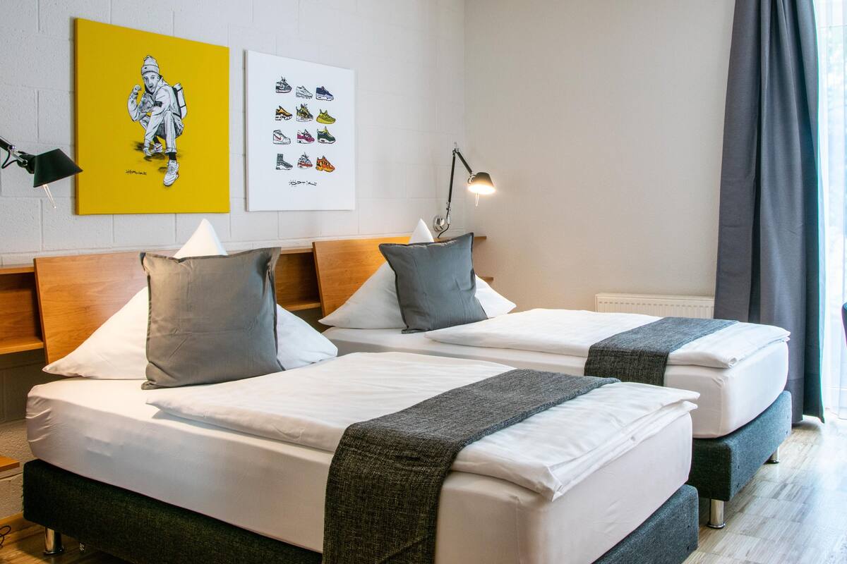 A hotel room with two beds, a desk, a chair, and artwork on the wall.