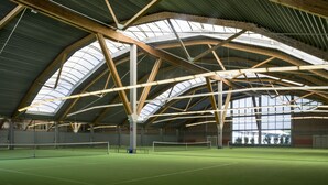 An indoor tennis court with a high ceiling and wooden beams. - IMPULSIV Hotel & Sportresort (Loerrach)