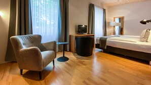 A hotel room with a checkered armchair, a bed, a TV on a wooden table, and a lamp. - IMPULSIV Hotel & Sportresort (Loerrach)