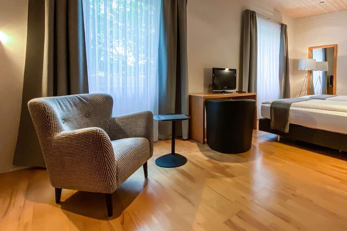 A hotel room with a checkered armchair, a bed, a TV on a wooden table, and a lamp.