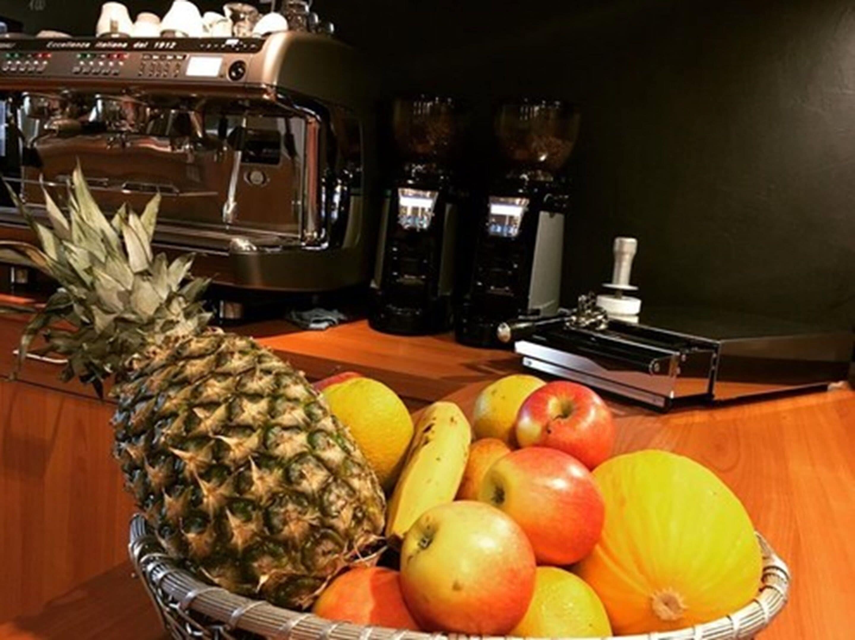 A kitchen counter with a fruit basket containing a pineapple, apples, and oranges.
