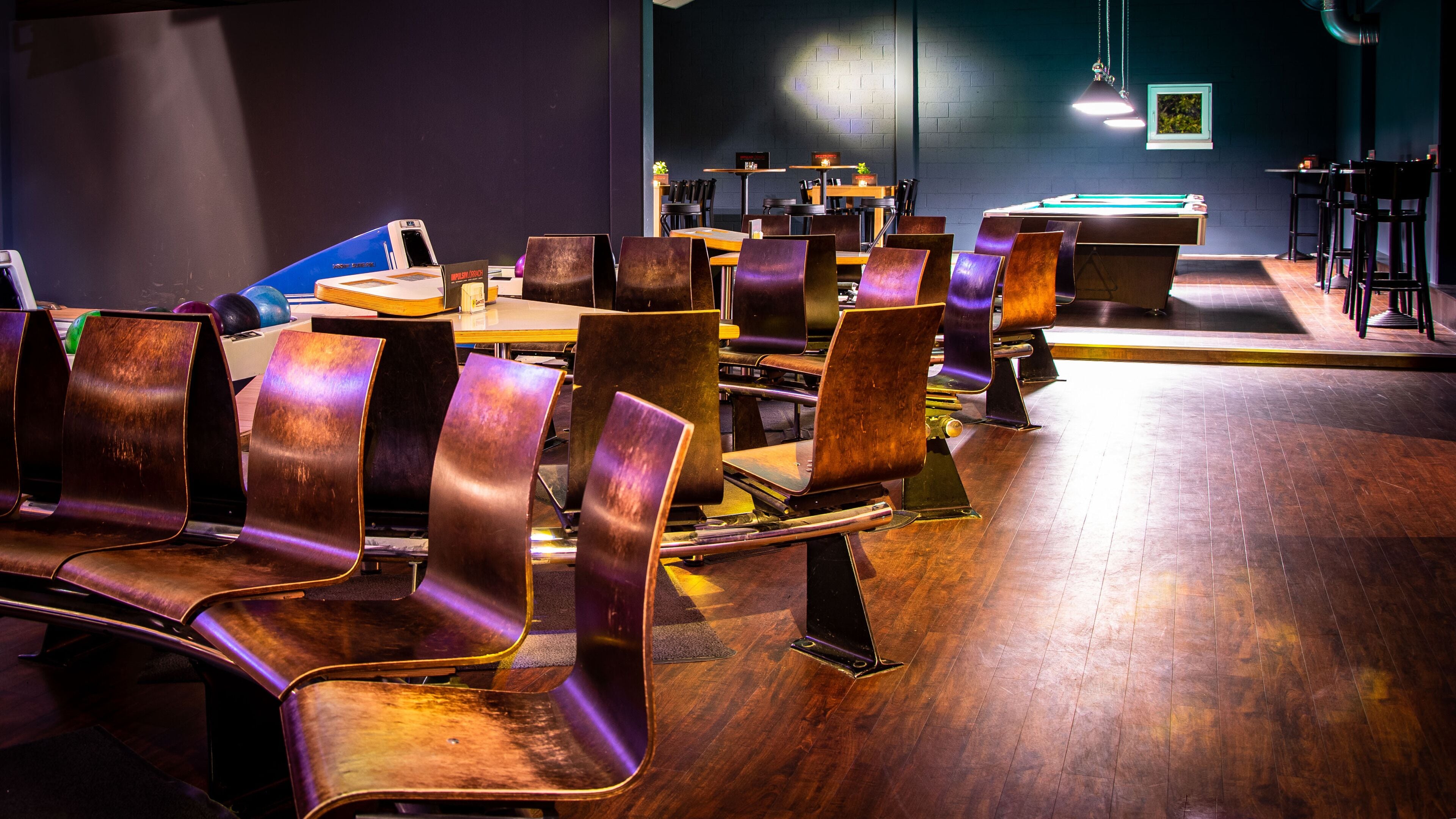 Un restaurante con mesas y sillas de madera, una mesa de billar y una pared oscura con un cuadro enmarcado.