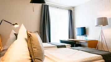A hotel room with two beds, a desk with a TV, a lamp, and a window with curtains.