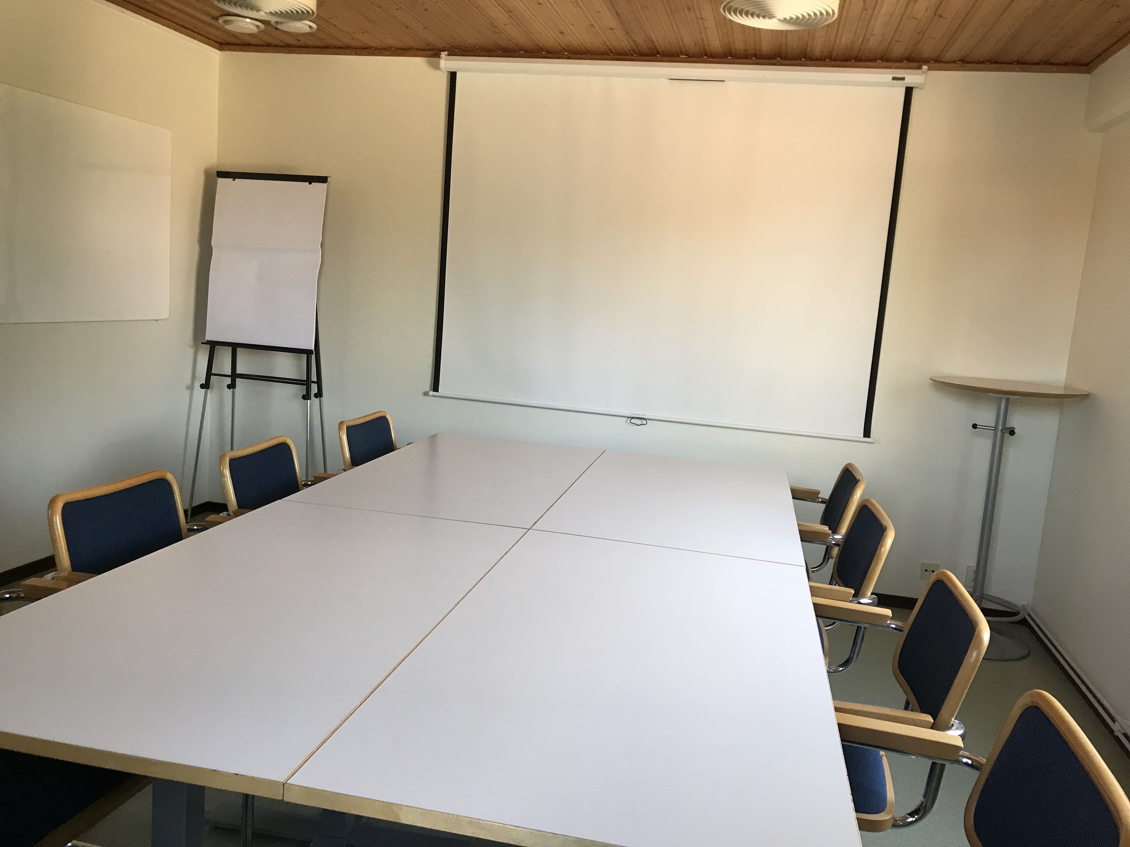 Una sala de conferències amb una taula gran, cadires, una pissarra i una pantalla de projector.