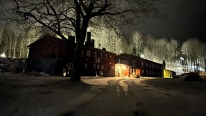 En snedækket gade om natten med en bygning med mange vinduer og et stort træ i forgrunden.