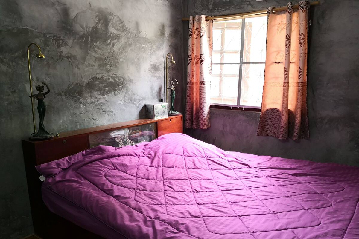 A room with a bed, a nightstand, a lamp, and a window with curtains.