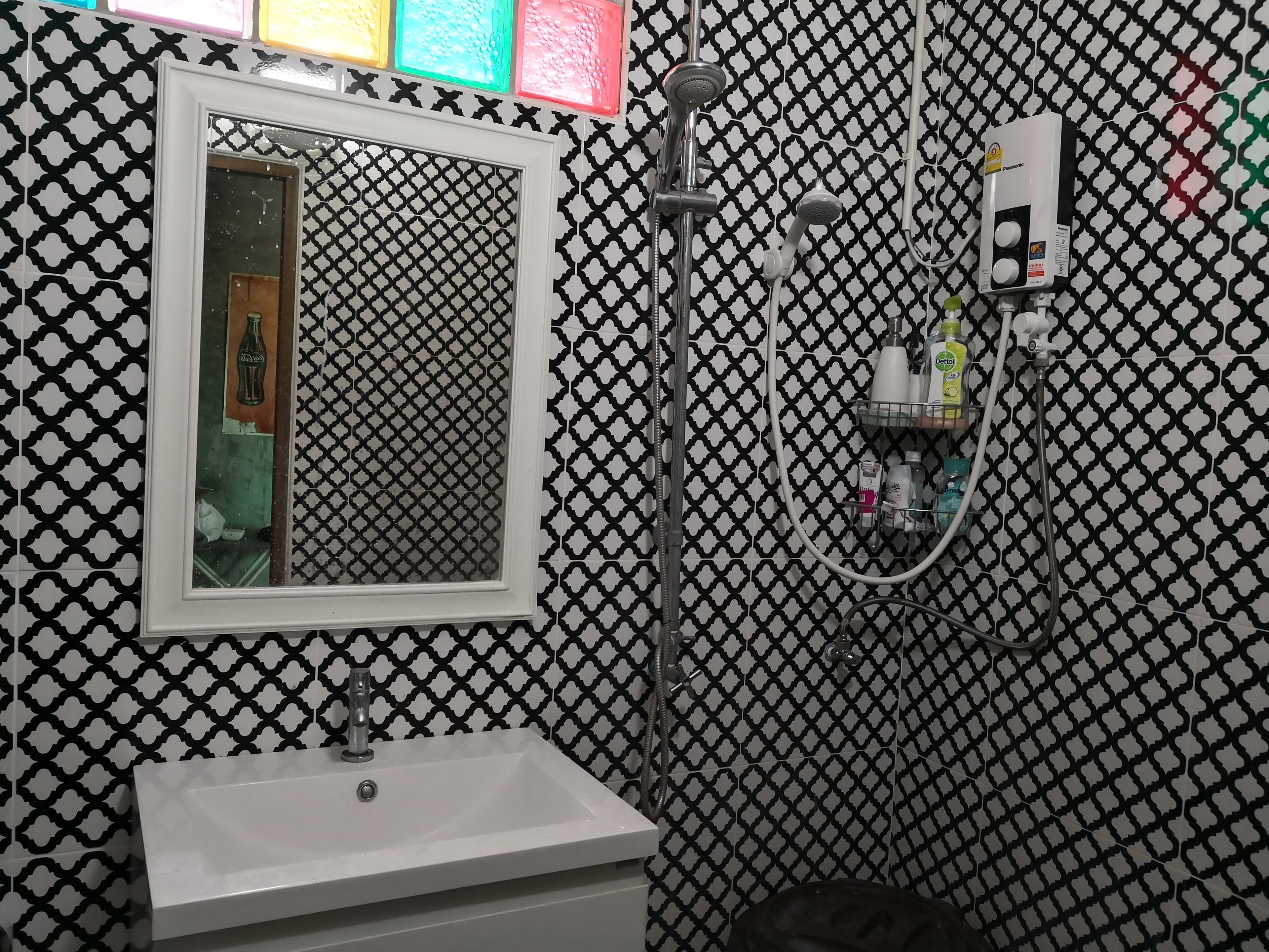 Een badkamer met een wastafel, spiegel, douche en een zeepdispenser aan de muur.