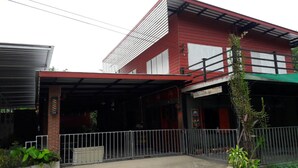 A red building with a covered patio area and a fenced front yard. - Baan Raiplaysoi Homestay (Photharam)