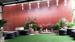 A patio area with artificial grass, tire seating, potted plants, and a decorative statue. - Baan Raiplaysoi Homestay (Photharam)