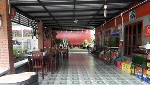 A covered outdoor area with a tiled floor, a table with chairs, and a variety of items on shelves. - Baan Raiplaysoi Homestay (Photharam)