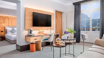 Una habitación de hotel moderna con una cama grande, un escritorio con televisión de pantalla plana, una mesita con un jarrón y vistas a las montañas a través de la ventana.