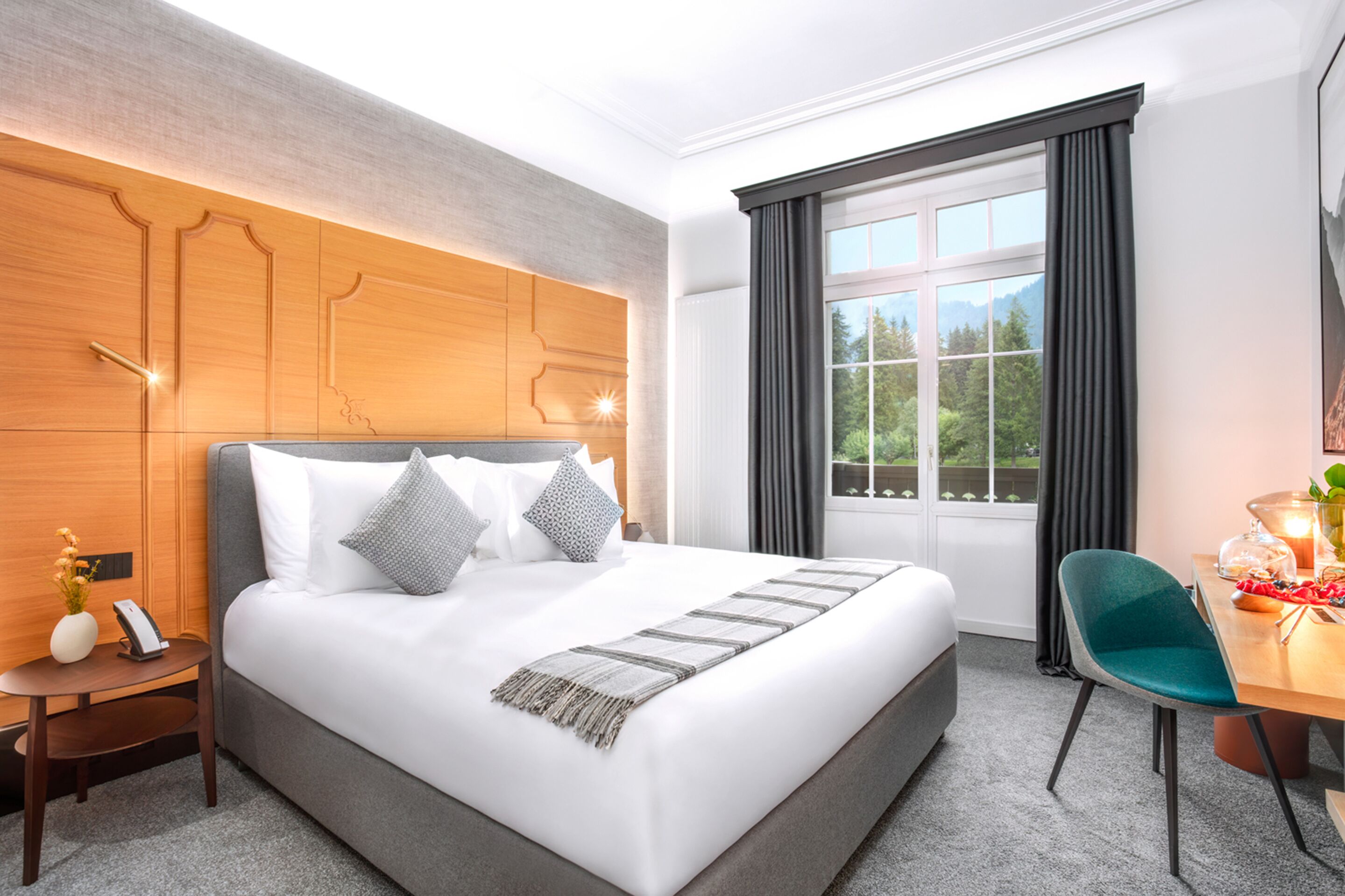 Ein Hotelzimmer mit einem großen Bett, einem hölzernen Kopfteil, einem Schreibtisch mit Stuhl und einem Fenster mit Vorhängen.