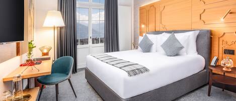 A hotel room with a large bed, a desk with a chair, a TV, and a window with curtains.