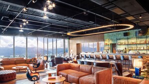A modern lounge area with leather sofas, a bar with a variety of bottles, and large windows offering a view of the mountains. - Villars Palace (Ollon)