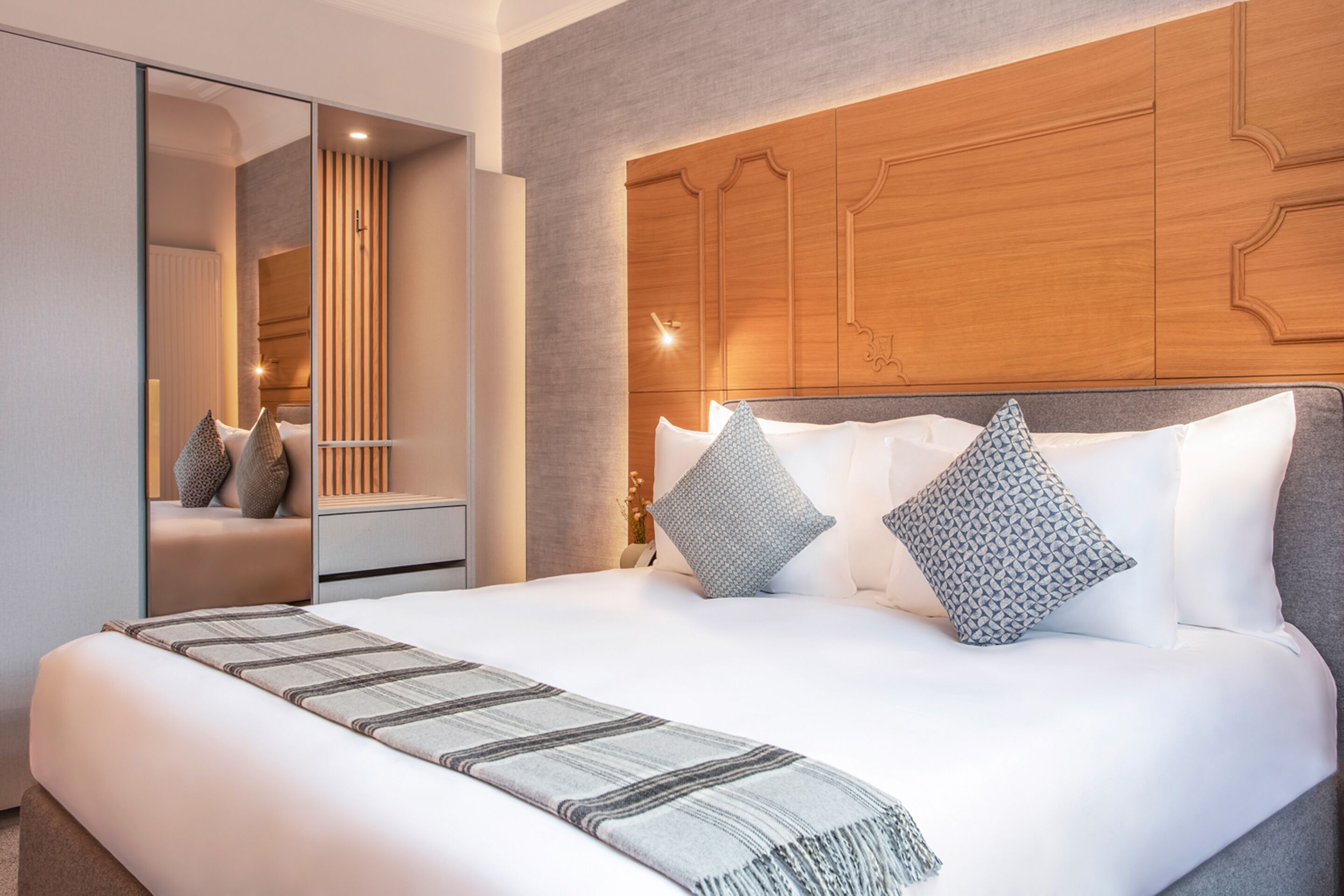 Une chambre d’hôtel moderne avec un grand lit, une tête de lit en bois et un miroir.
