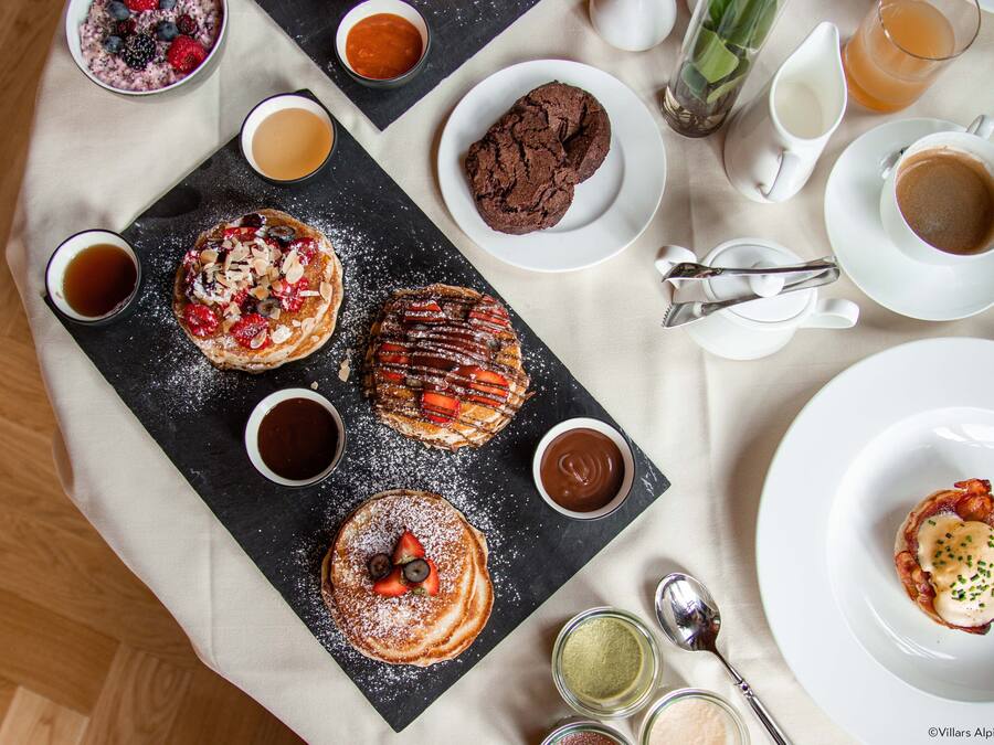 Ein Frühstücksarrangement mit Pfannkuchen, Waffeln und Gebäck auf einer Schieferplatte, dazu Tassen Kaffee und Tee.