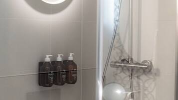 Ein modernes Badezimmer mit einer Glaskabine zur Dusche, einer Wandleuchte und drei Toilettenartikeln.