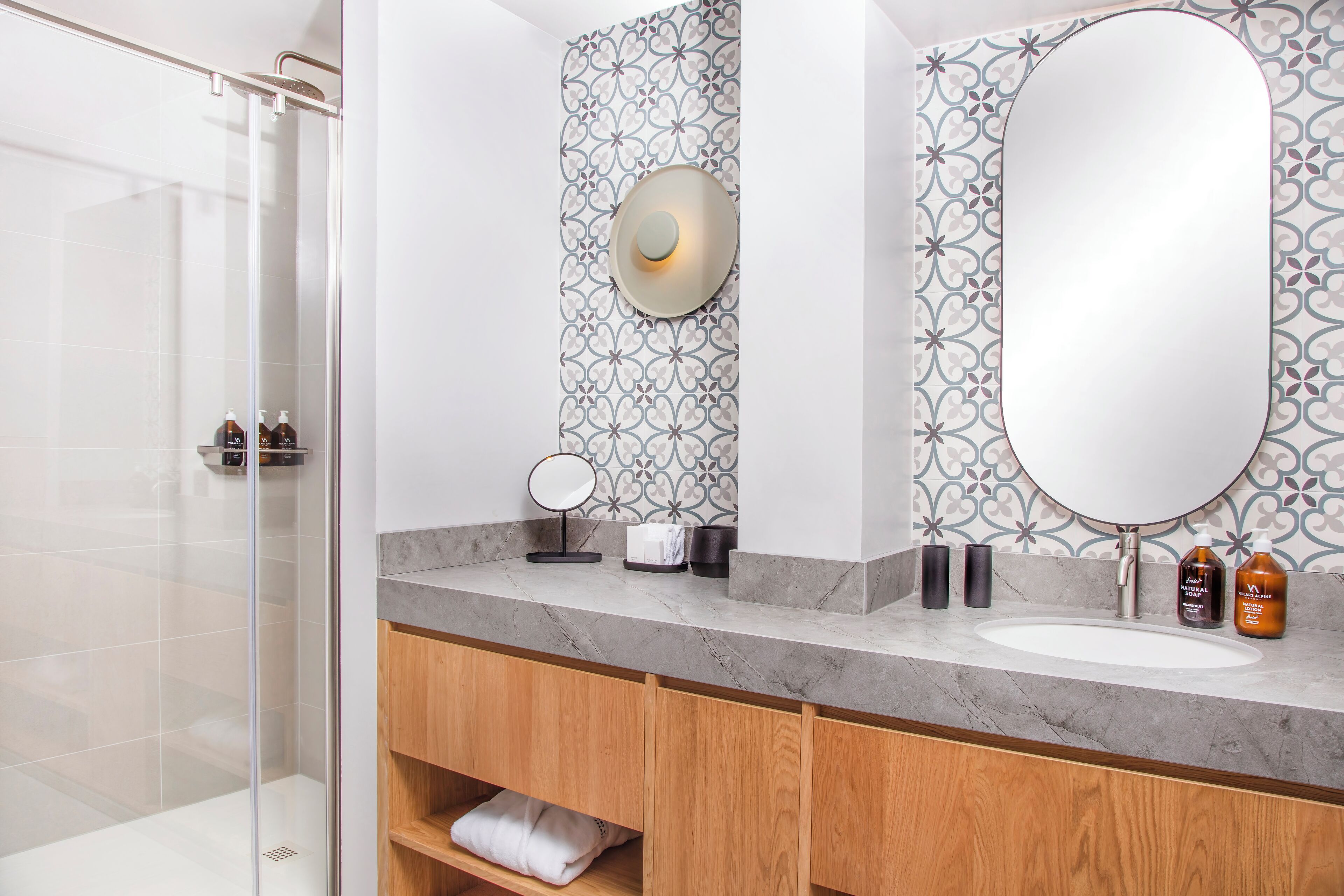 A modern bathroom with a glass shower enclosure, a marble sink, and patterned wall tiles.