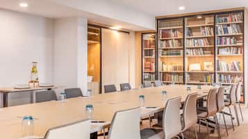 Un salón de conferencias con una larga mesa, sillas y una estantería llena de libros.