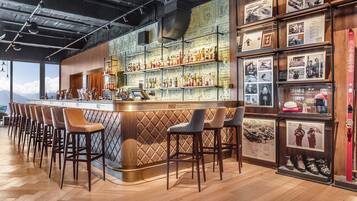 Una zona de bar con taburetes de madera, estantes con botellas y cuadros en la pared.