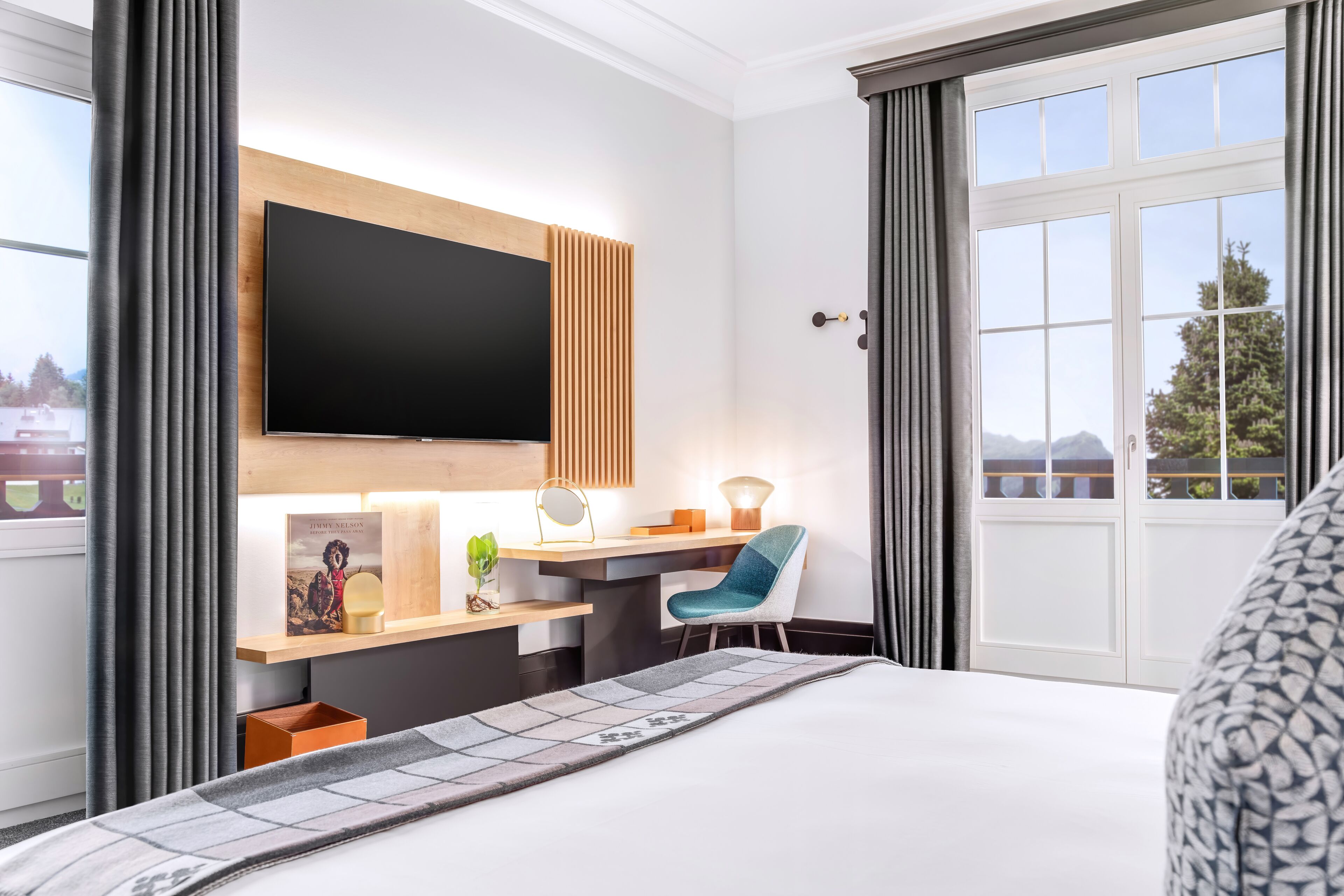 Camera d'albergo con un grande letto, una scrivania con televisione a schermo piatto, una poltrona e una finestra con tende.