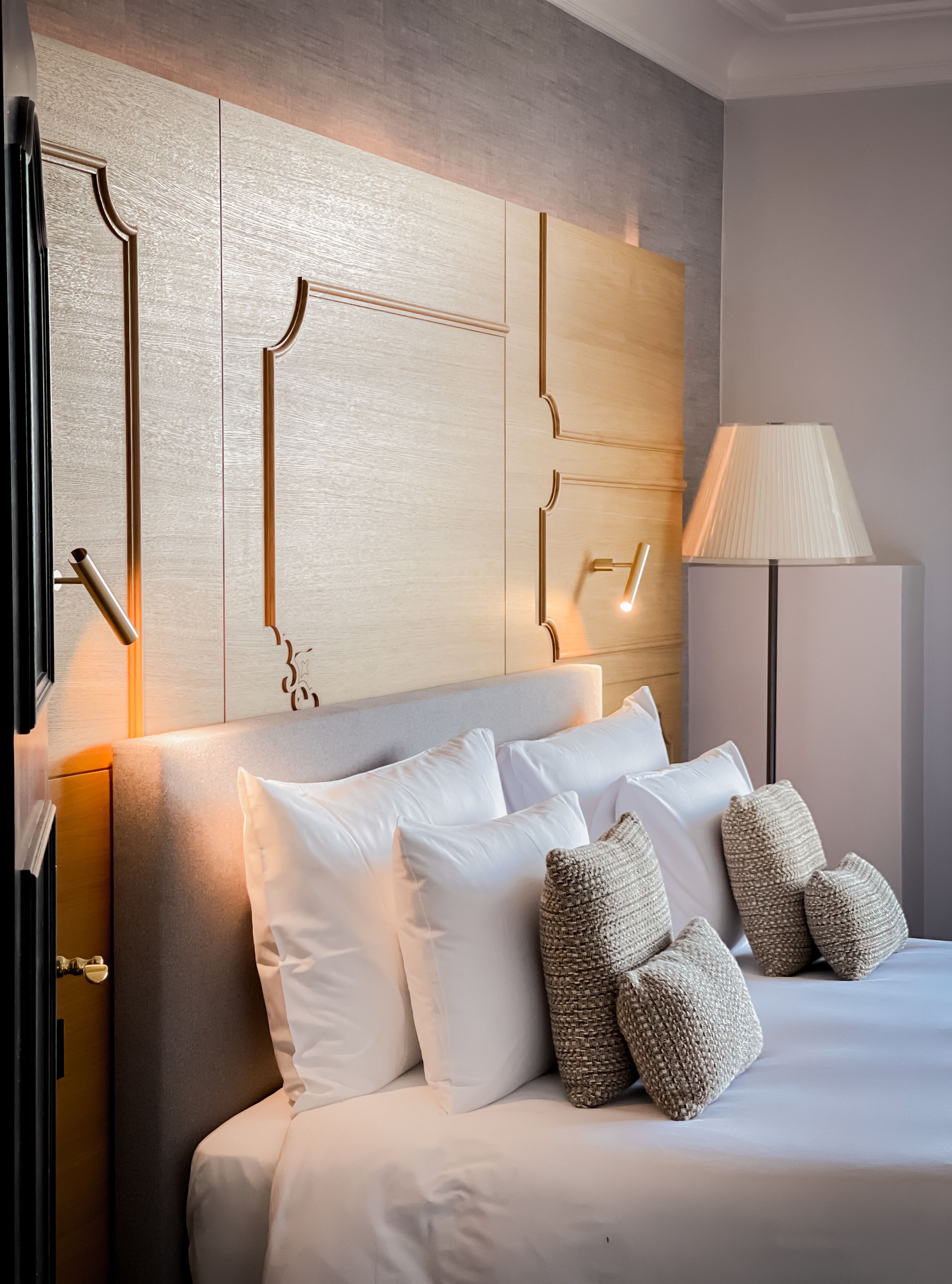 A modern hotel room with a large bed, white bedding, and a wooden headboard with built-in lighting.