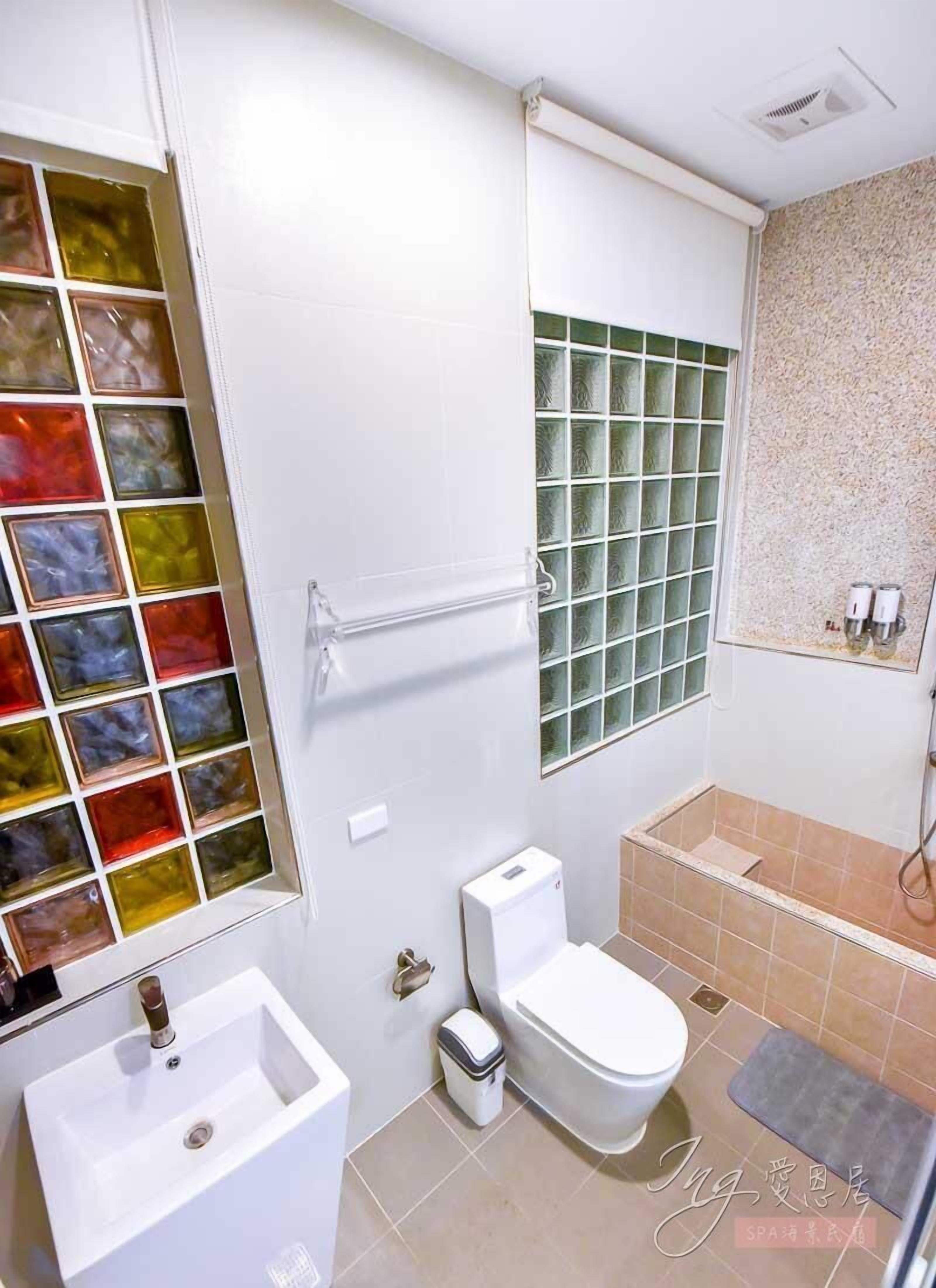 A bathroom with a white sink, toilet, and bathtub. There is a window with colorful glass panes and a shower area with a tiled wall.