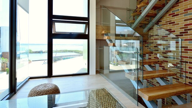 Un intérieur moderne avec un escalier en verre, une vue sur l’extérieur et un banc en bois.