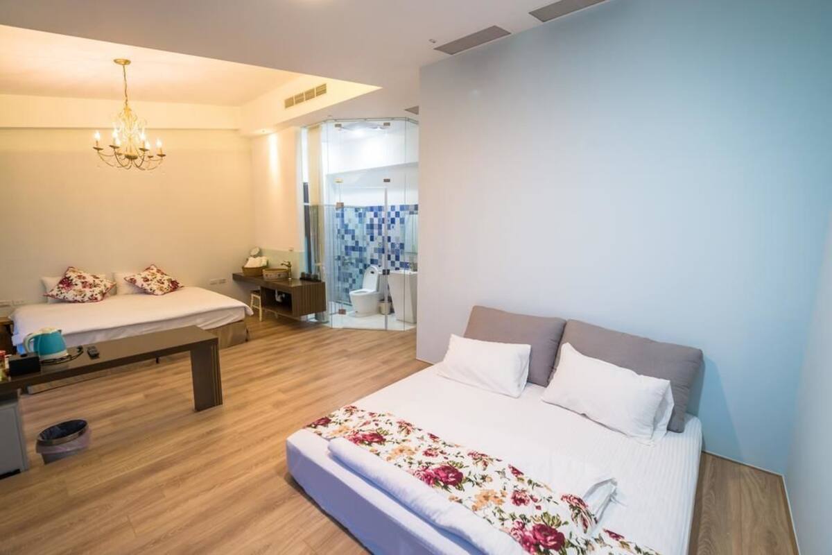 A modern bedroom with a large bed, a bedside table, a desk, and a shower area.