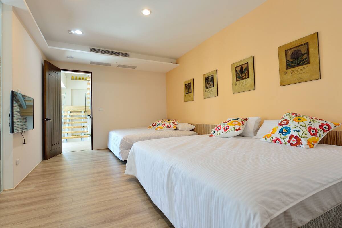 A hotel room with two beds, a wooden floor, a door leading to a balcony, and framed botanical prints on the wall.