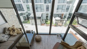 Un salon moderne doté d’une grande porte vitrée donnant sur un balcon, d’un canapé agrémenté d’un ours en peluche, d’une petite table et d’un panier décoratif.